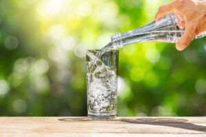 Person gießt Wasser aus einer Flasche in ein Glas